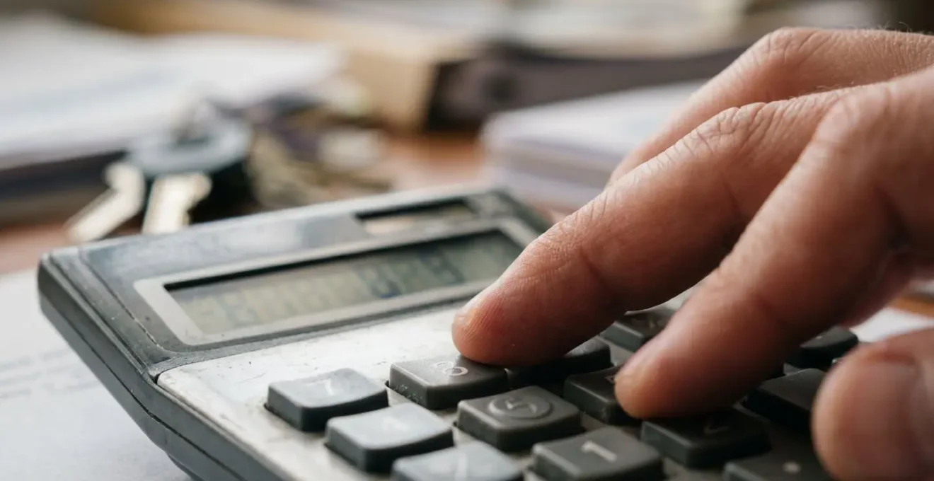 Personne utilisant une calculatrice avec des papiers d'assurance auto flous en arrière-plan